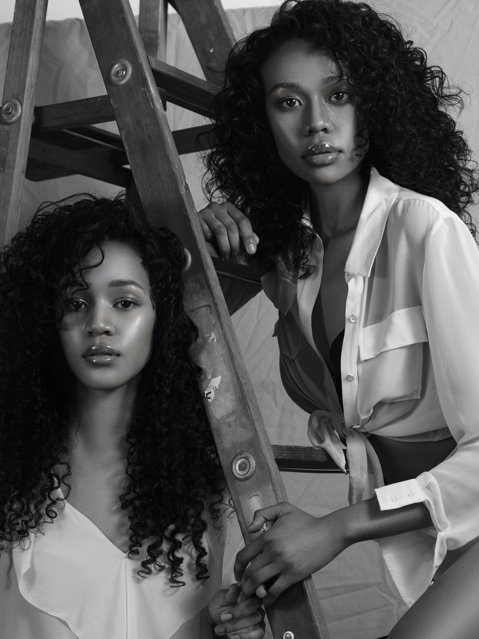 Black-and-white fashion portrait of two women beside a ladder